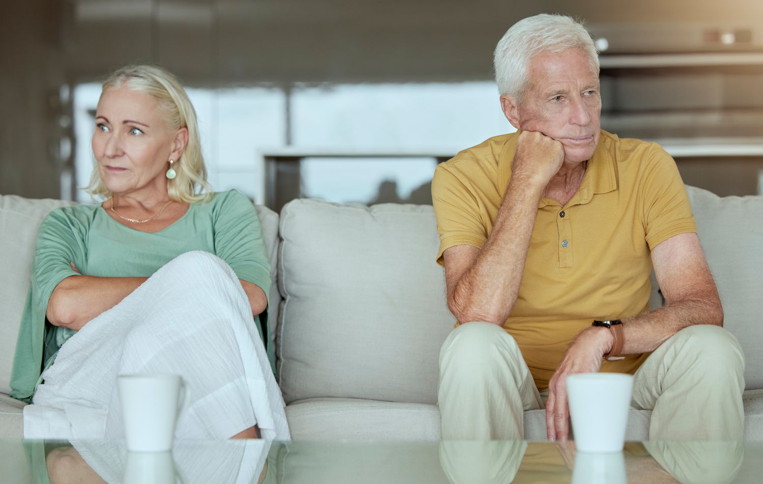 Older couple with a reverse mortgage together sitting far apart from each other after a discussion of divorce.