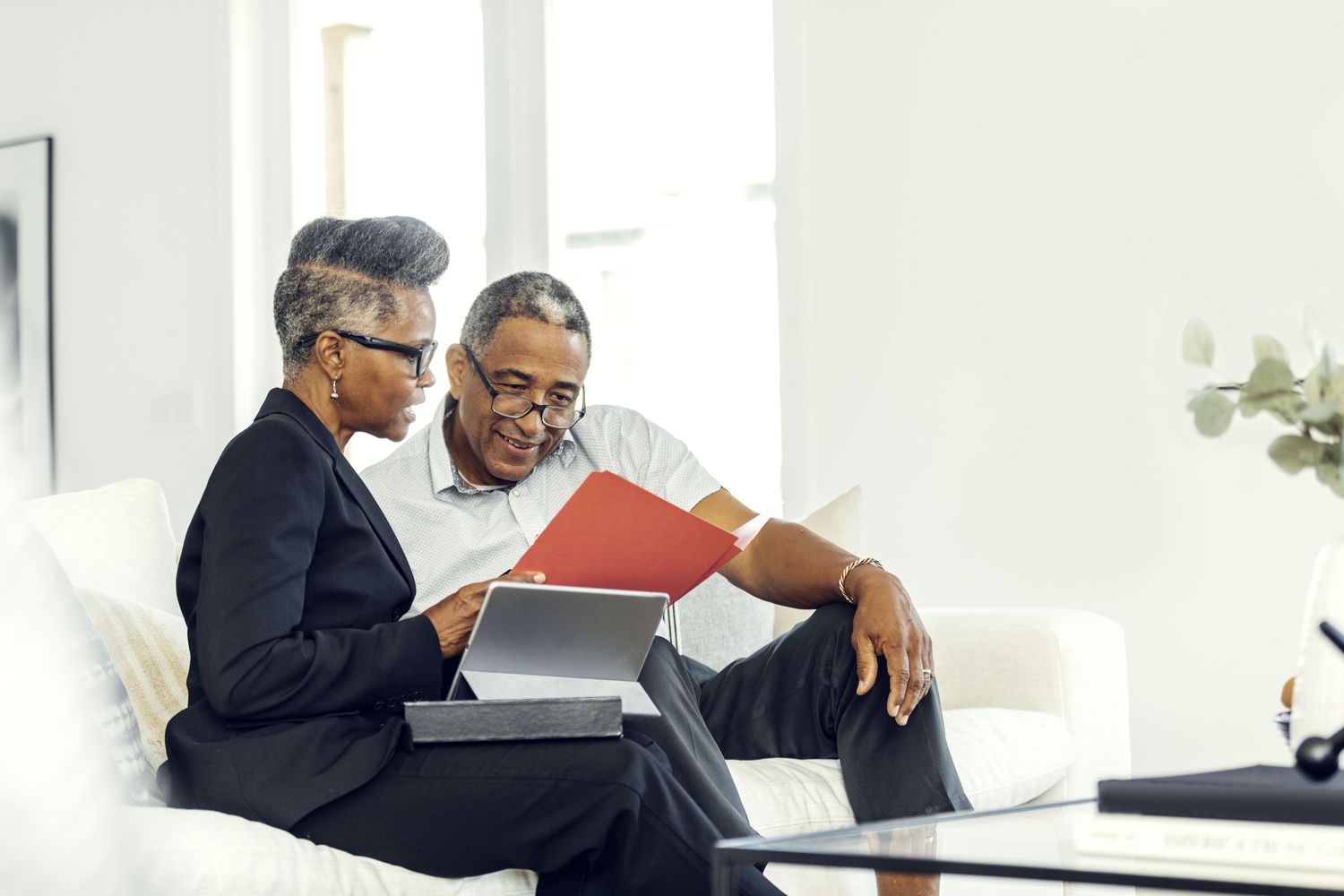 Two people seated on a couch, looking at portfolio records and tax forms.
