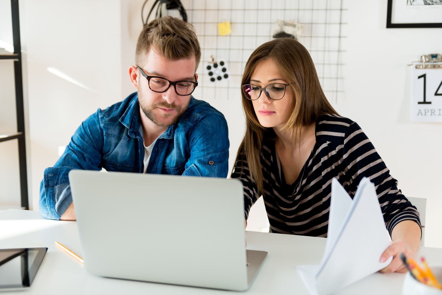Young couple at their kitchen table, looking together at a laptop and documents