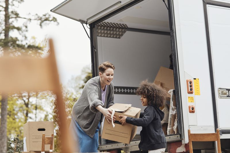 Woman handing box from moving truck to small chlid.