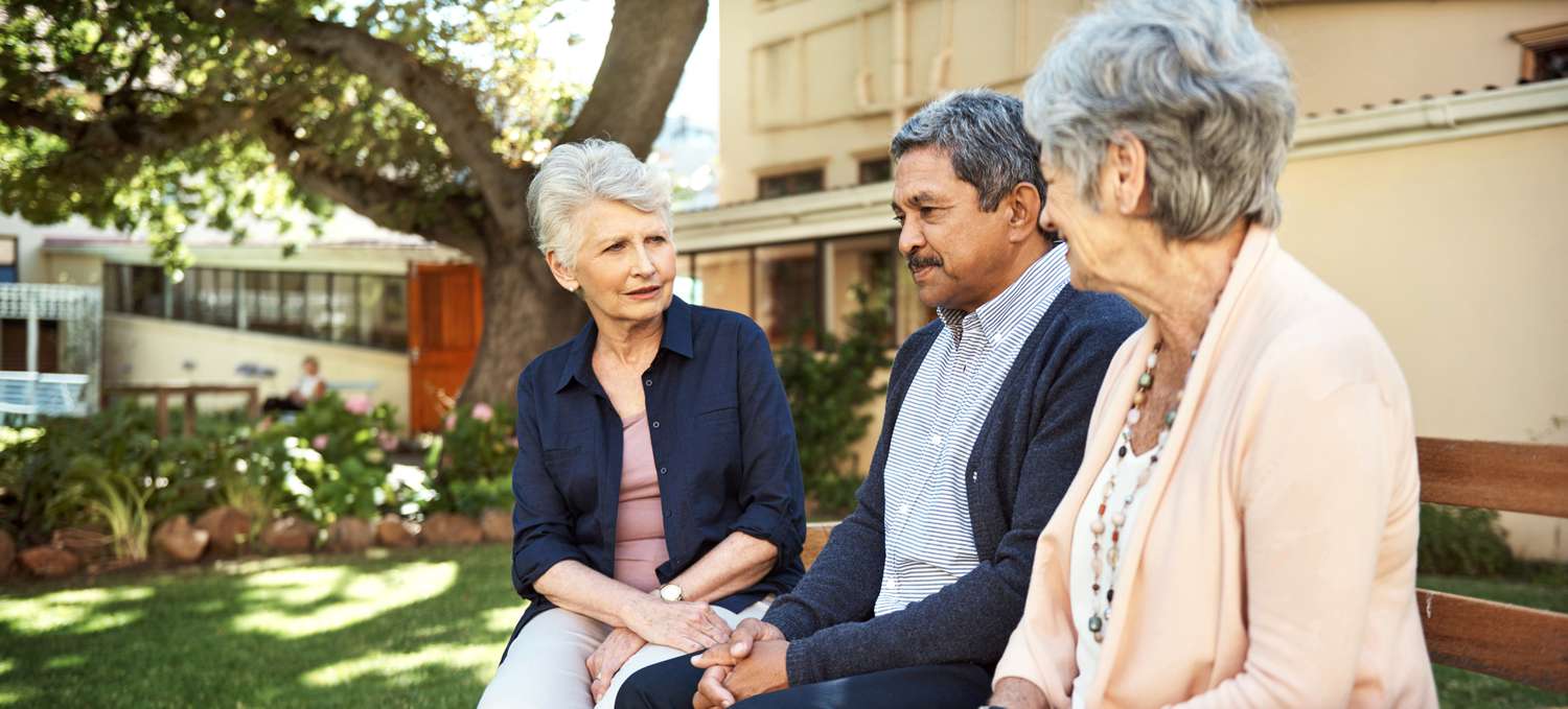 Shot of a group of older friends sitting together on a bench out in a community garden.