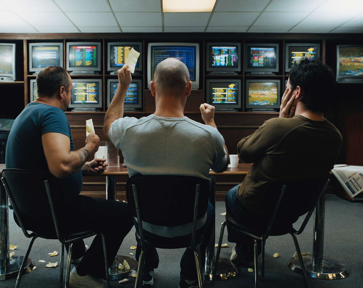Three men in a betting shop with TVs showing various live betting events