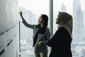Two women discussing something on a white board.