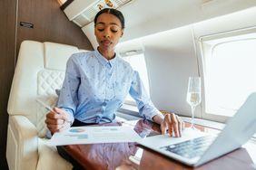 A woman working on a laptop and writing on a document while in a private jet