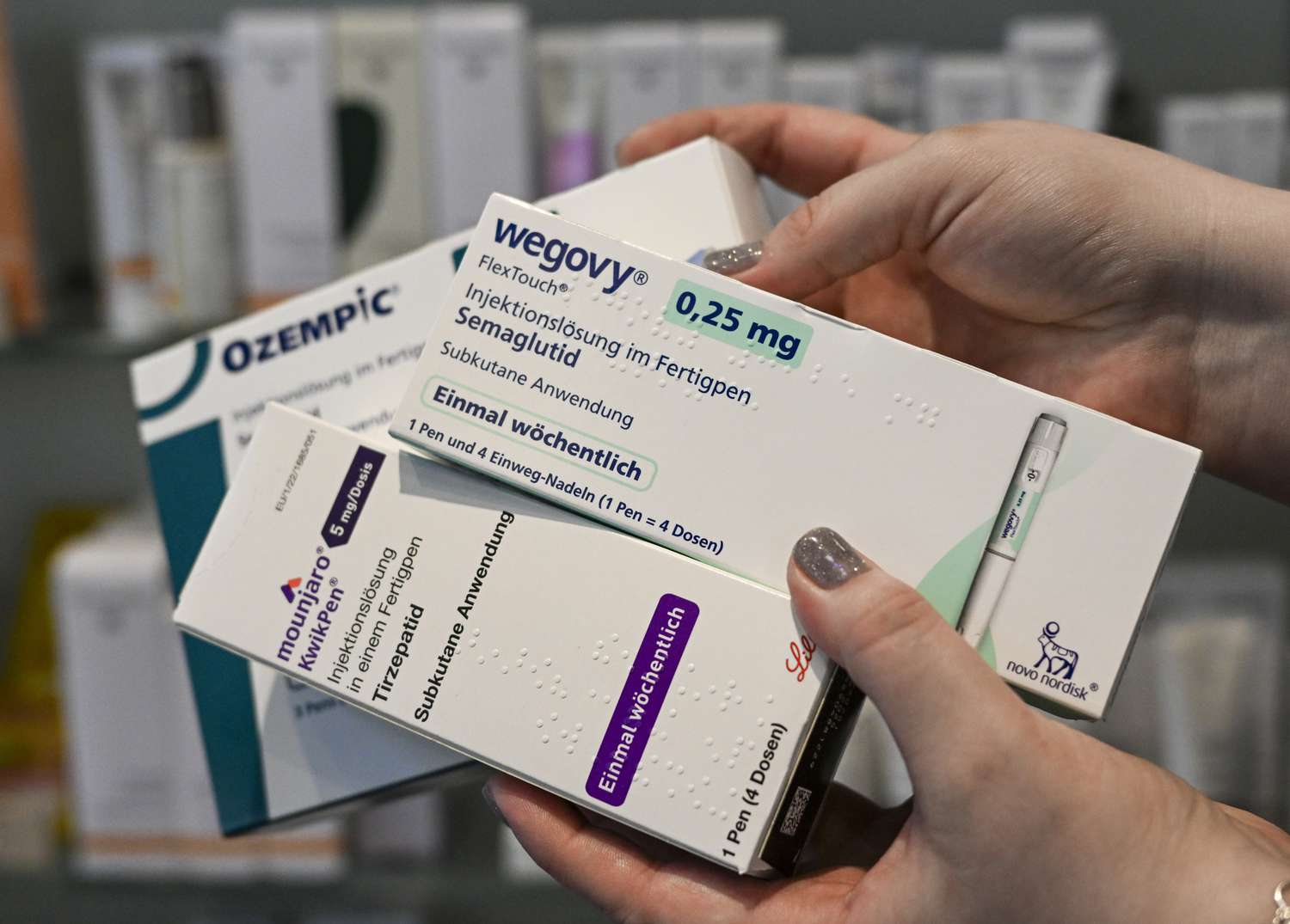 A person holds prescription medication boxes for Wegovy, Ozempic, and Mounjaro at a pharmacy.