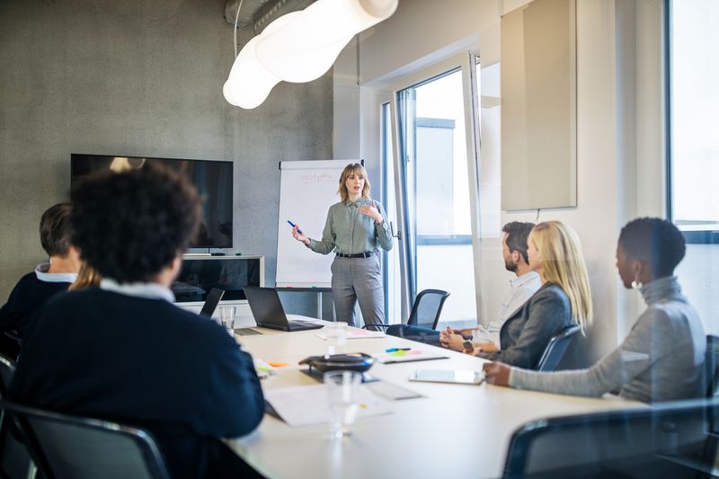 Businesswoman addressing a meeting around board table with colleagues.