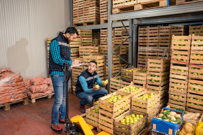 Two workers in a warehouse full of fresh fruits and vegetables