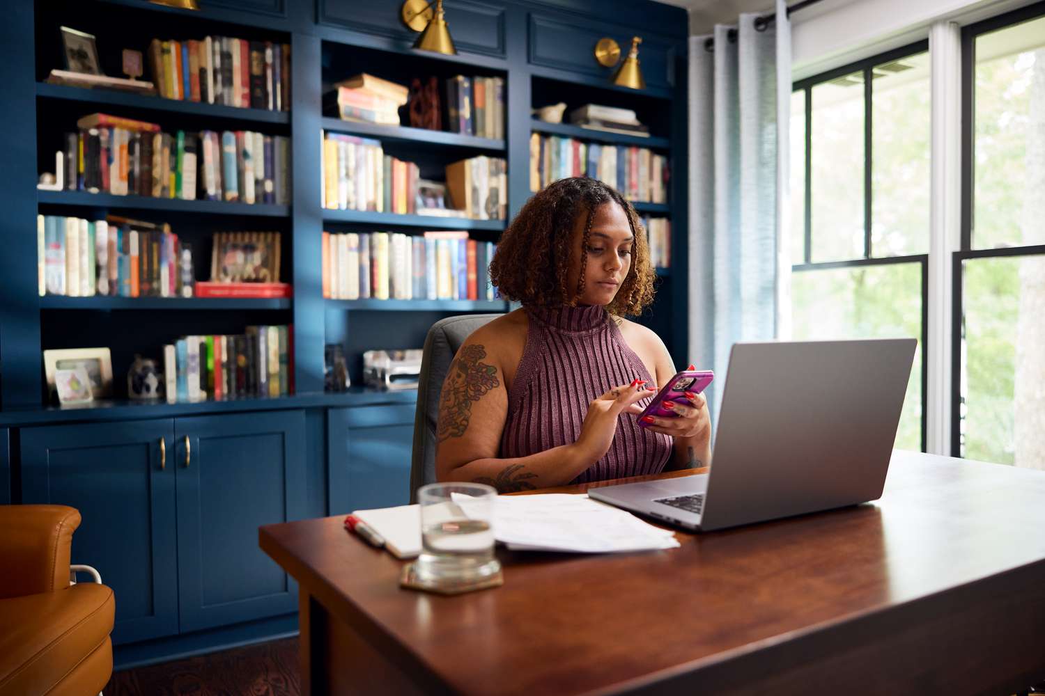 A person sits in a home office while closes checking account on the phone.