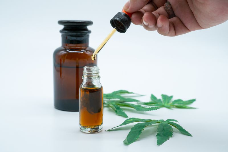 Hand holding bottle of Cannabis oil in pipette isolated on white.