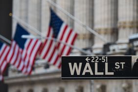 A Wall Street sign appears in front, with three American flags hanging in the background.