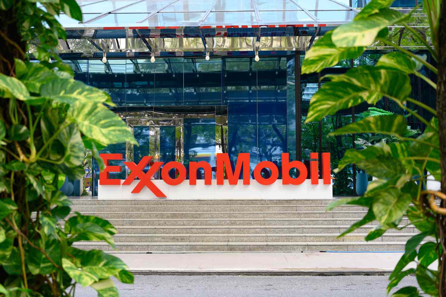 The red ExxonMobil logo is seen on a sign outside an office building, with green plants on both sides.