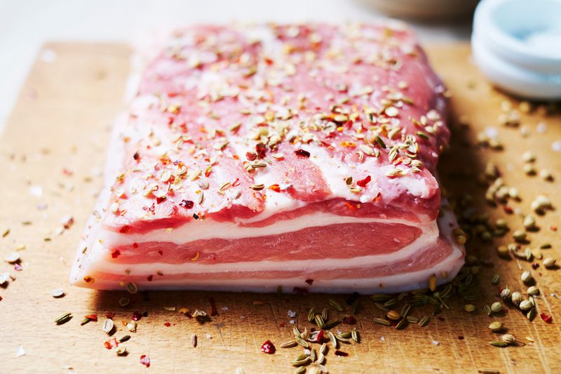 A pork belly prepped for cooking with coriander and fennel seeds and flaked chili.