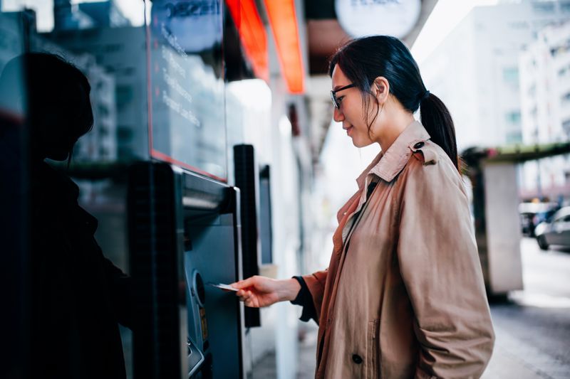 A young woman inserts her card into an ATM on a city street.