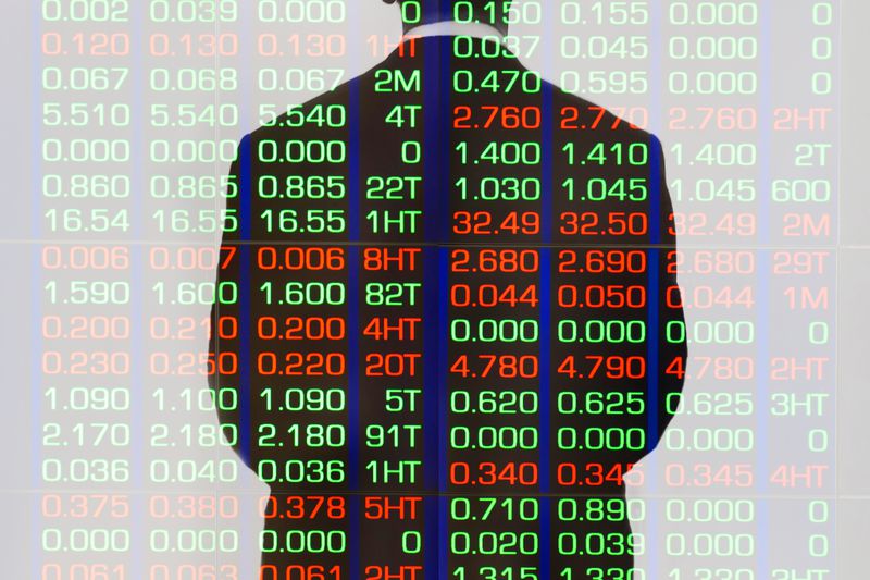 Businessperson in a silouette standing against a stock market display.