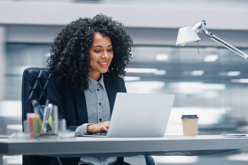 A woman sits at a desk with a laptop and coffee cup