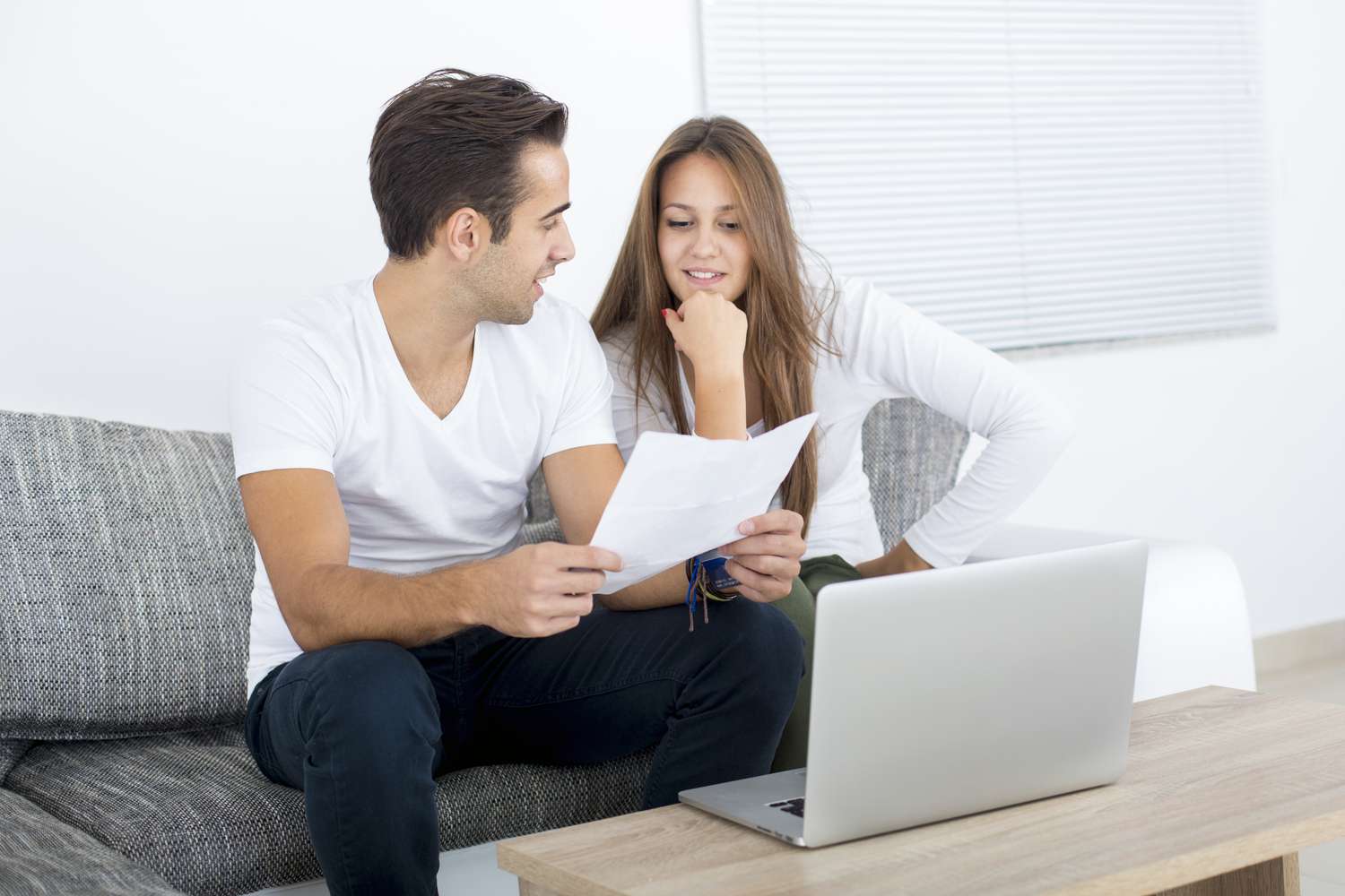 Young couple sitting on their sofa and looking together at mortgage rates on a laptop