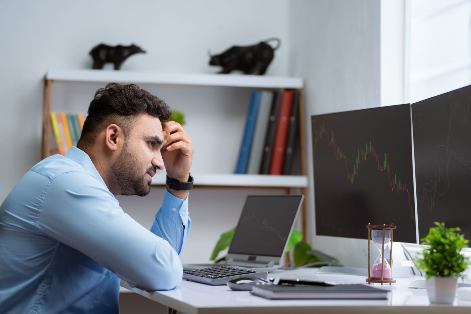 A frustrated retail investor stares at a computer monitor and scratches their forehead as they wait for a trade order on a thinly traded stock to execute. 