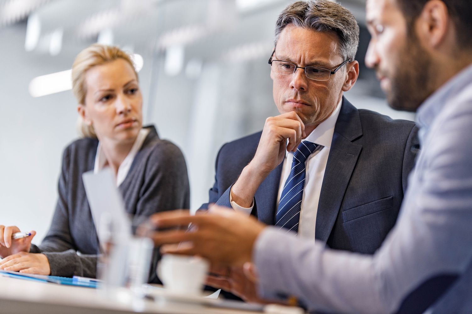 A concerned business owner looks at a document and talks to advisors about how to avoid a hostile takeover. 
