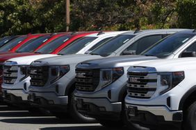 Several GMC trucks sit in a row in a dealership parking lot.