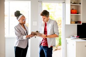 A man signing a contract on a clipboard in front of a woman
