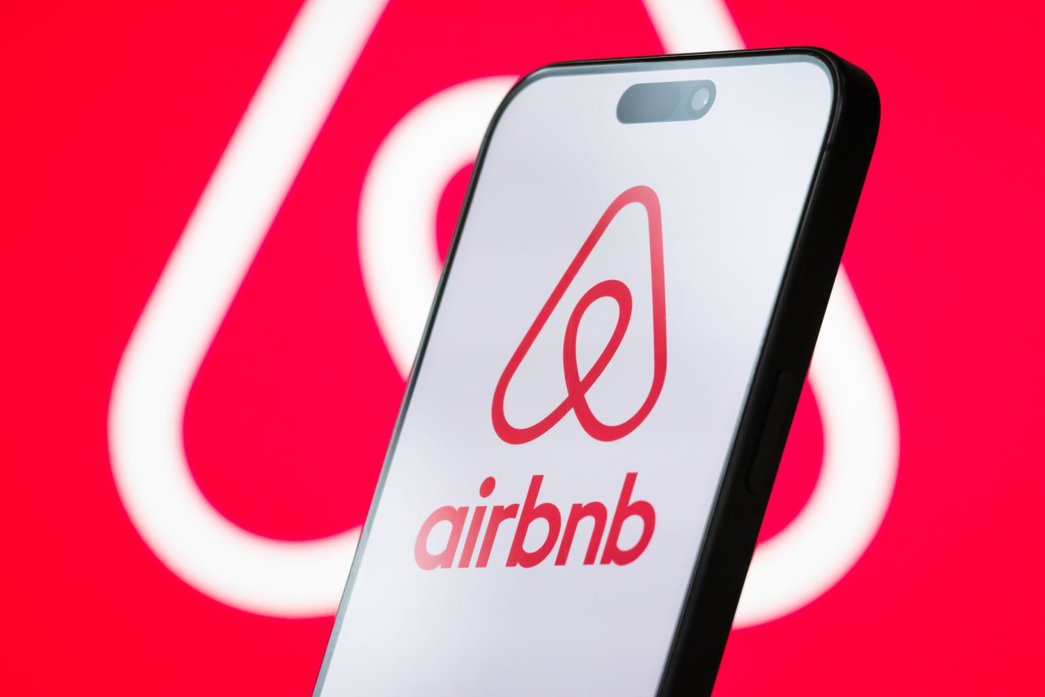 The logo of Airbnb, Inc. is displayed on a smartphone screen, with the company's branding visible in the background