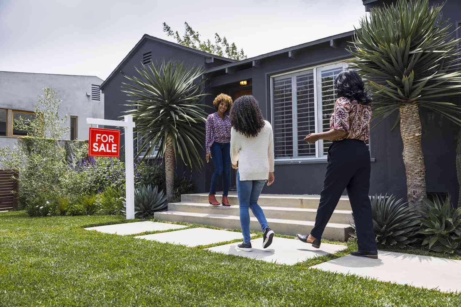 Home buyers greet a real estate agent outside of a house for sale. 