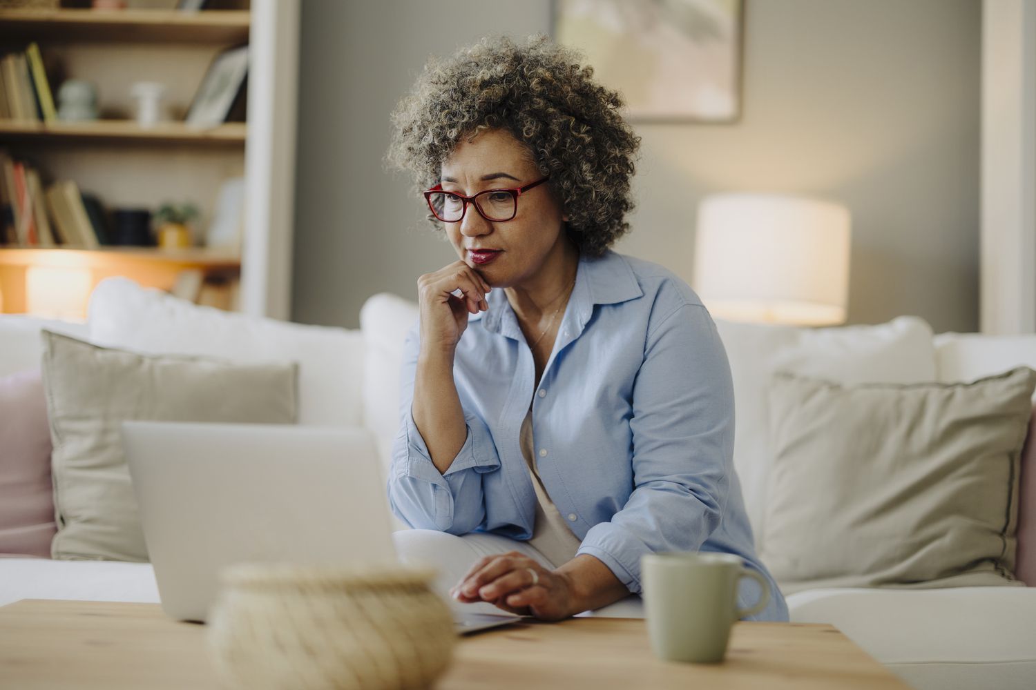 A woman sits on a couch looking at a laptop on the coffee table